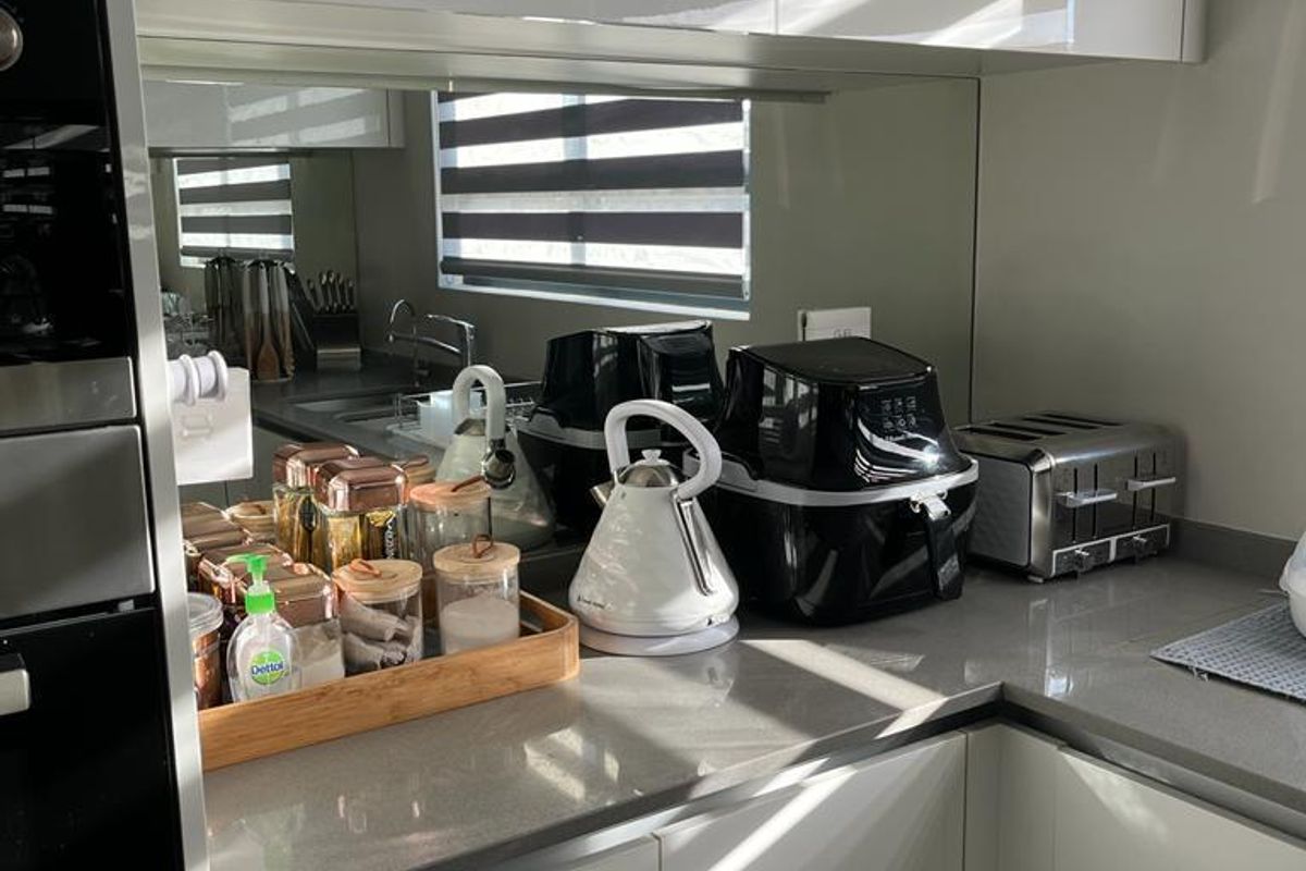 Modern kitchen featuring sleek white cabinetry, stone countertops, and a mirrored splashback, creating a bright and contemporary culinary space.