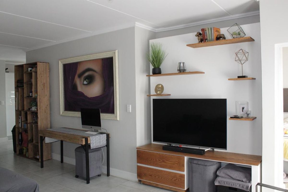 A well-maintained living area featuring built-in shelving units and a dedicated workspace area with neutral wall finishes and tiled flooring.