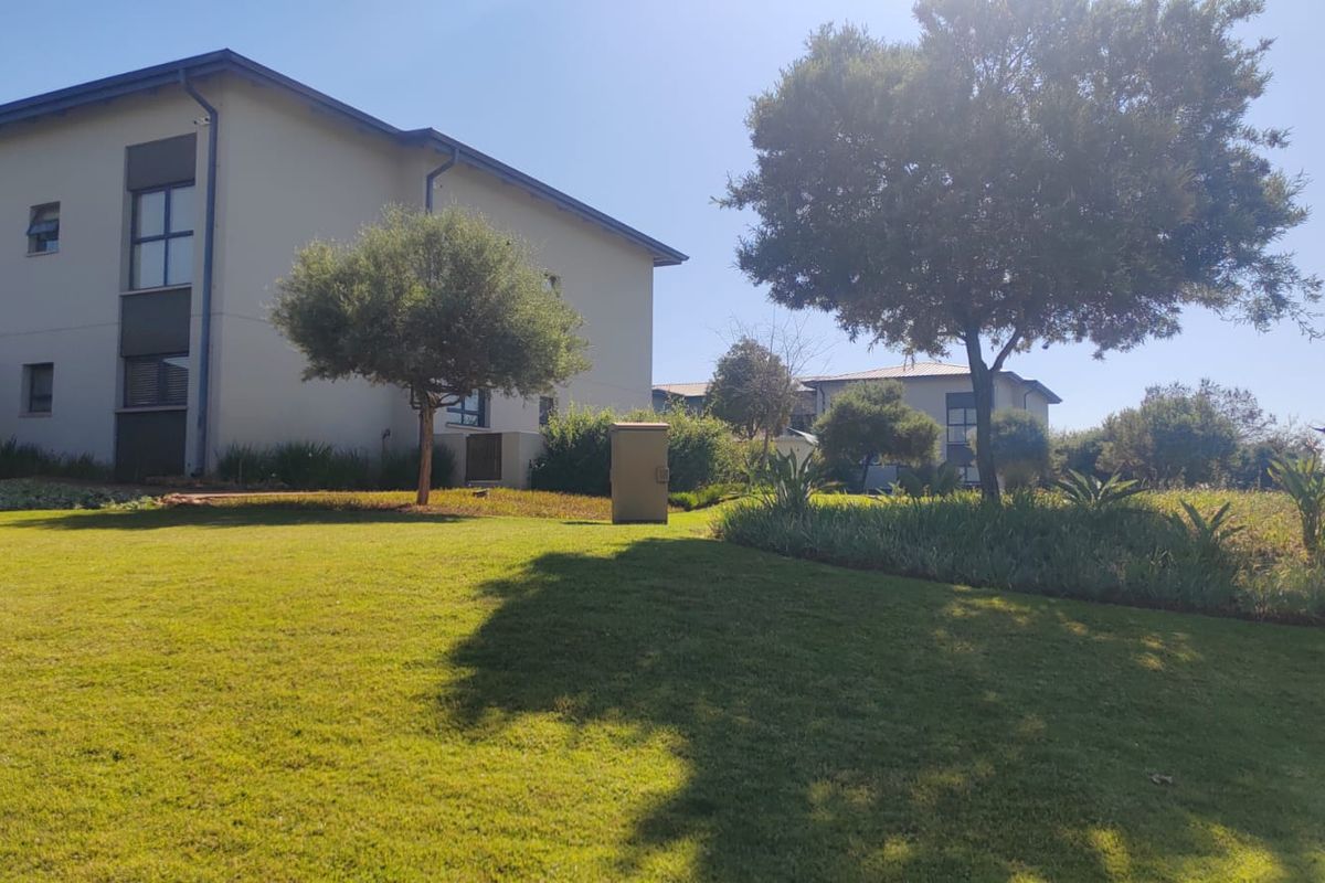 A view of the apartment complex exterior featuring a well-maintained lawn and landscaped garden area.