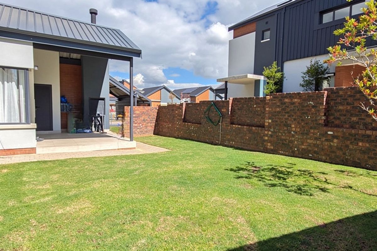 A well-maintained rear garden featuring a paved patio area, a built-in braai, and a perimeter brick wall, offering a private outdoor space.