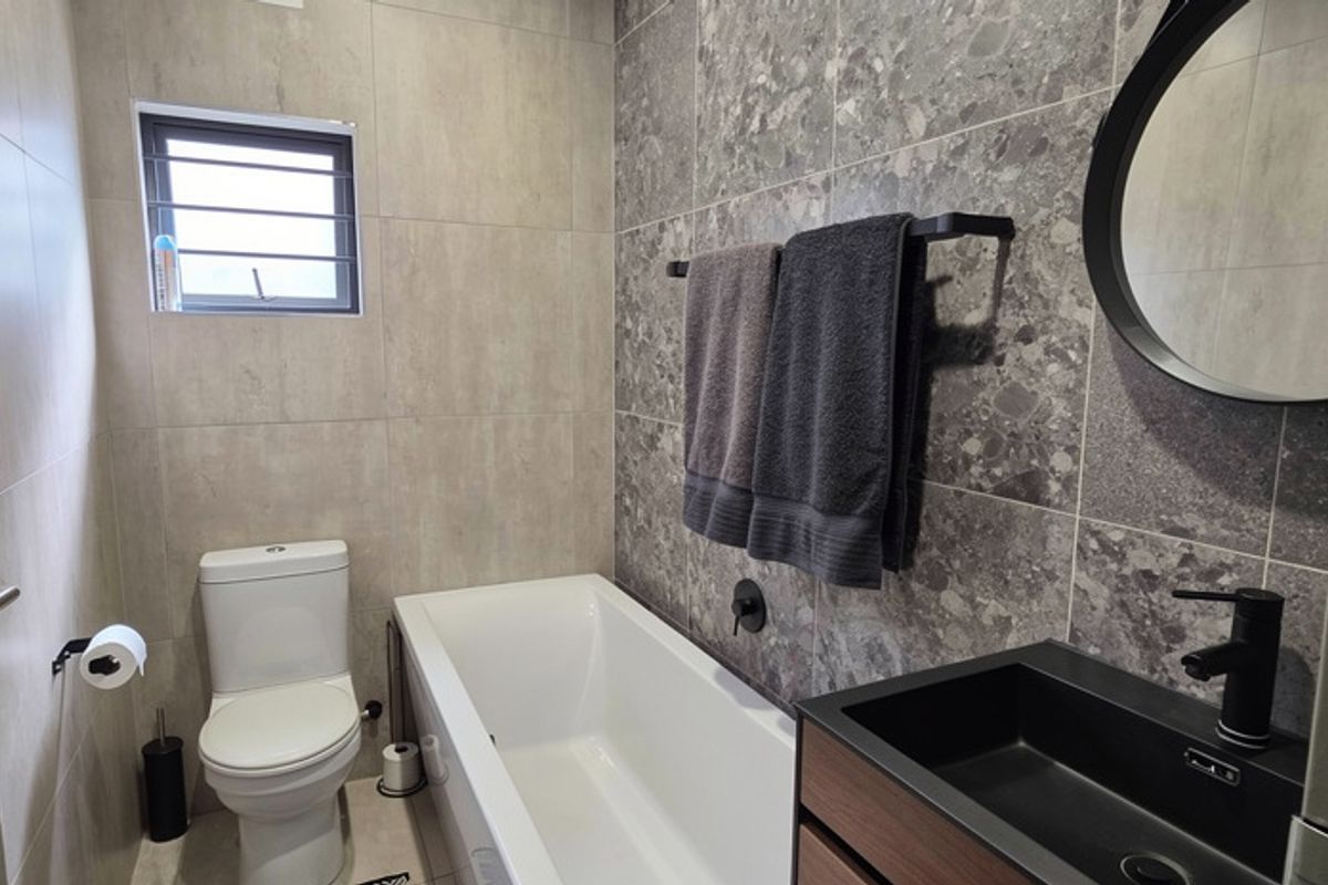 Modern bathroom featuring a built-in bathtub, wall-mounted vanity with integrated basin, matte black fixtures, and contemporary grey tiled walls.