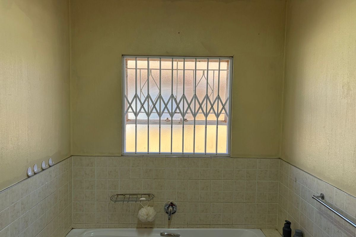 A functional bathroom featuring a built-in bathtub with wall-mounted mixer and a window fitted with a security gate.