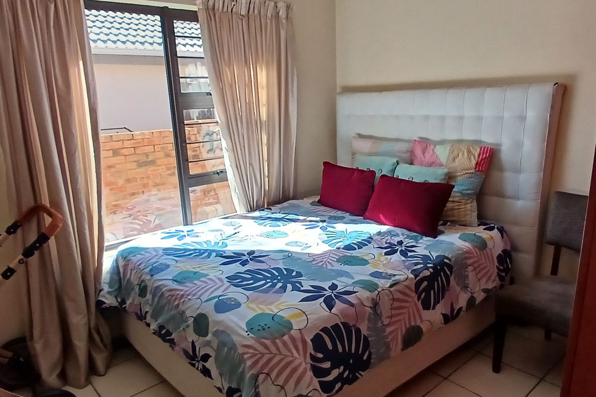 A standard bedroom featuring tiled flooring and a large window with security bars, providing natural light and access to the exterior.