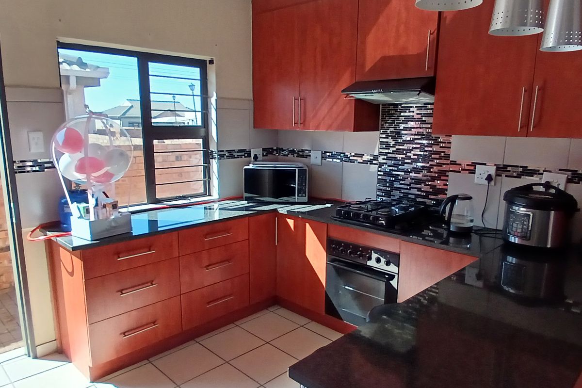 A functional kitchen featuring wood-finish cabinetry, dark granite countertops, a built-in oven, gas hob, and a mosaic tile backsplash.