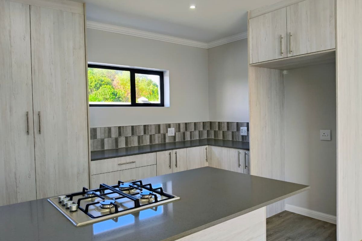 Modern kitchen featuring light wood-grain cabinetry, dark stone countertops, a central island with a built-in gas hob, and a tiled backsplash.