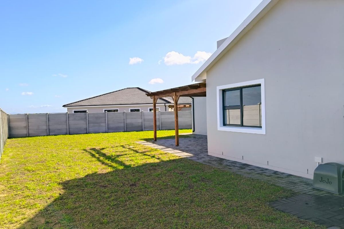 A view of the rear garden featuring a paved patio area with a wooden pergola and a perimeter boundary wall.