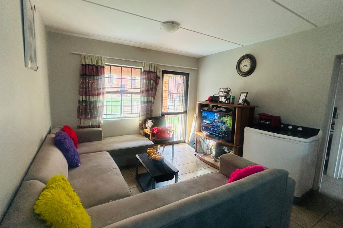 A functional living room featuring tiled flooring, a large window with security bars, and direct access to an outdoor area.