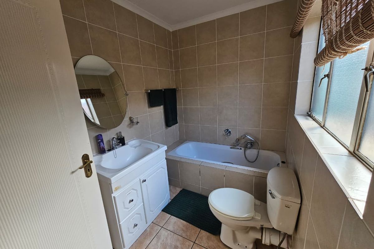A compact bathroom featuring floor-to-ceiling wall tiles, a built-in bathtub, a vanity basin, and a standard toilet.