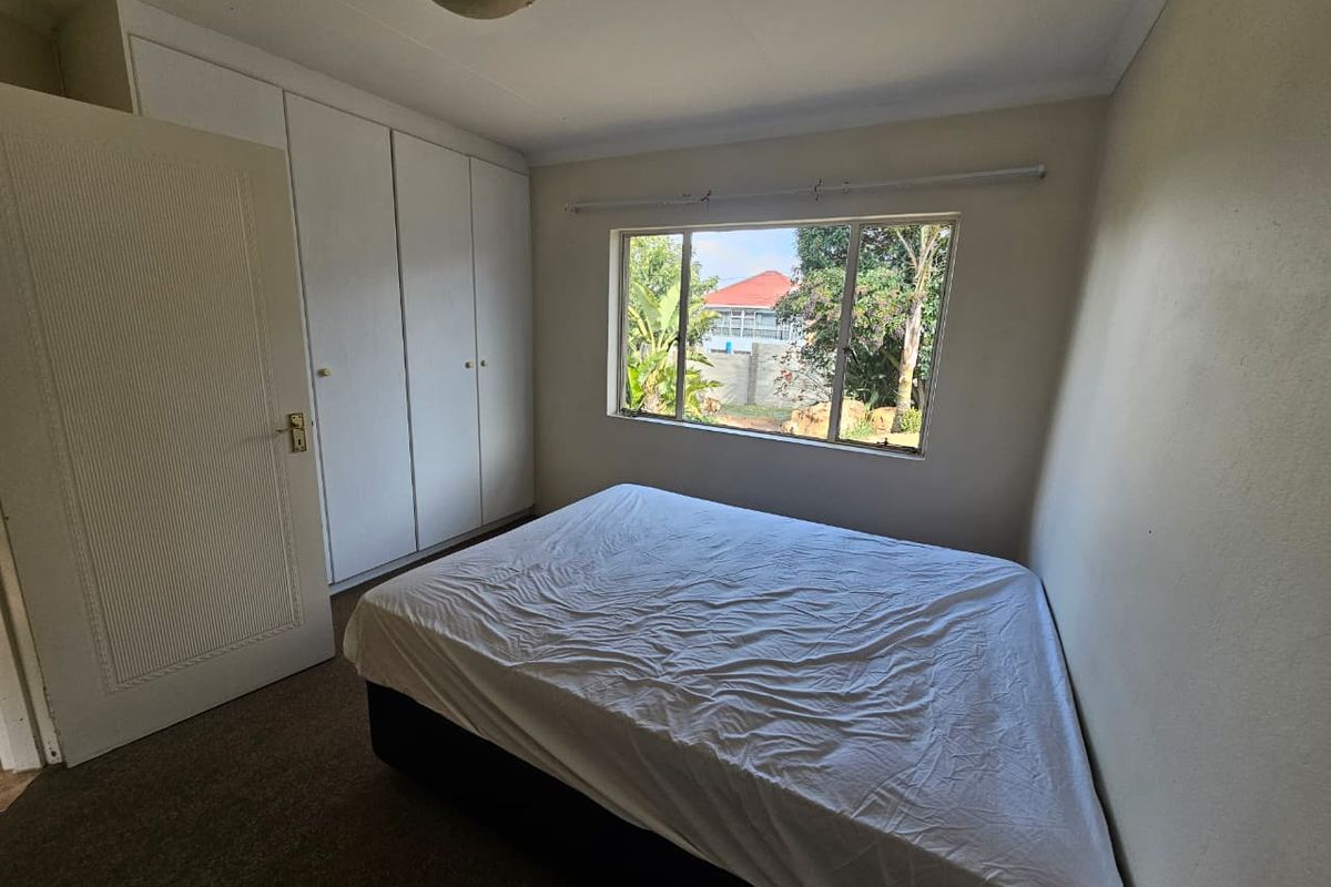 A bedroom featuring built-in cupboards and a window overlooking the garden area.