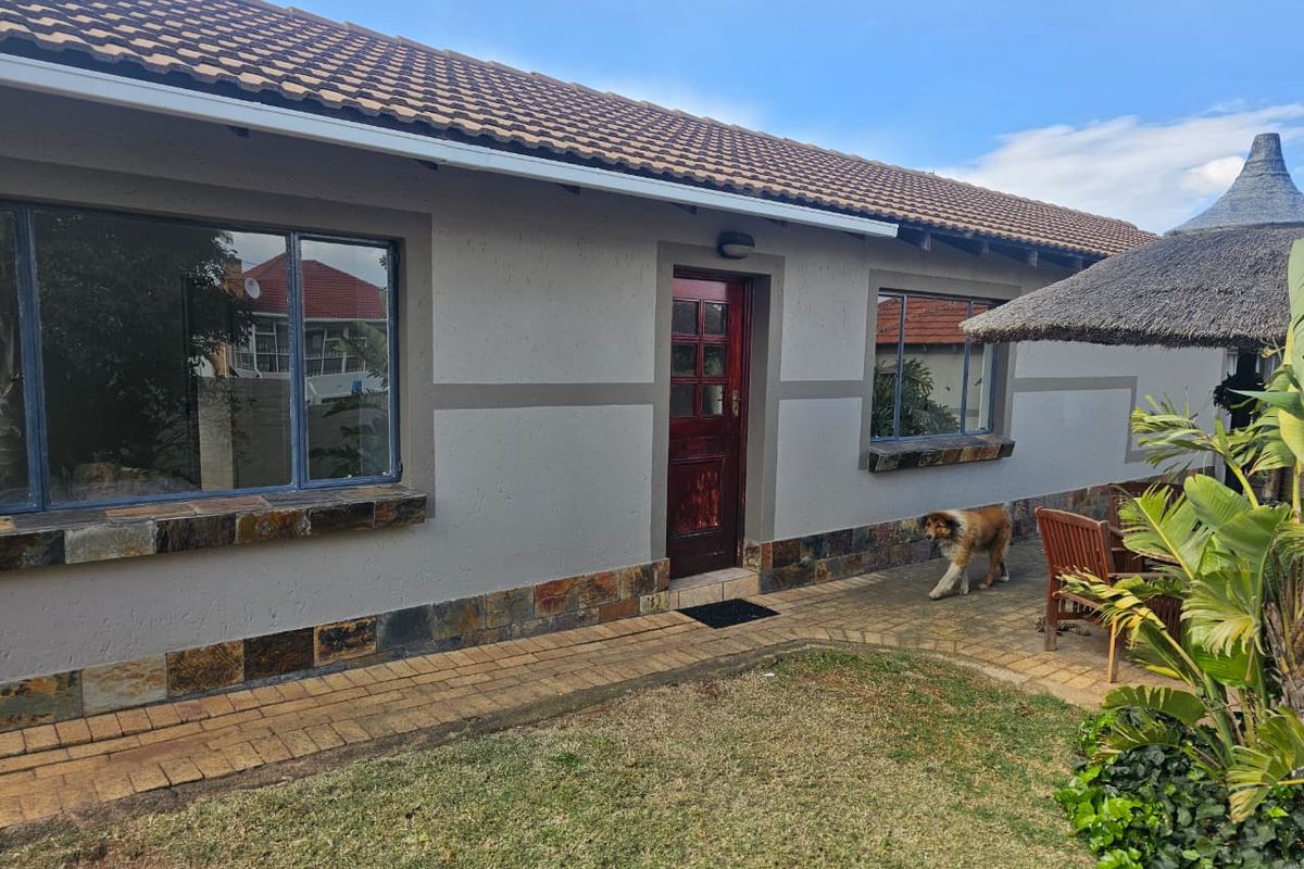 Rear view of the cottage featuring a paved patio area, tiled roof, and stone-clad base detailing.