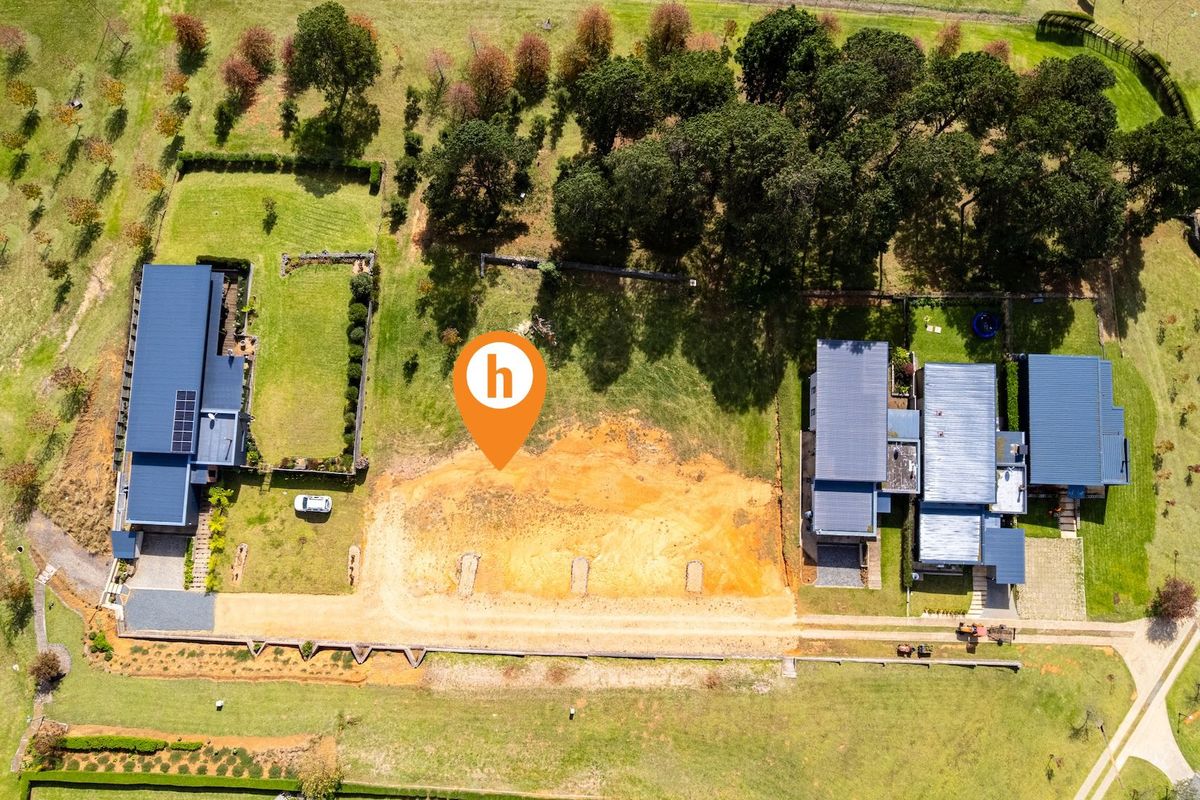 Aerial view of a vacant residential plot situated between existing properties, featuring cleared earth and established surrounding landscaping.