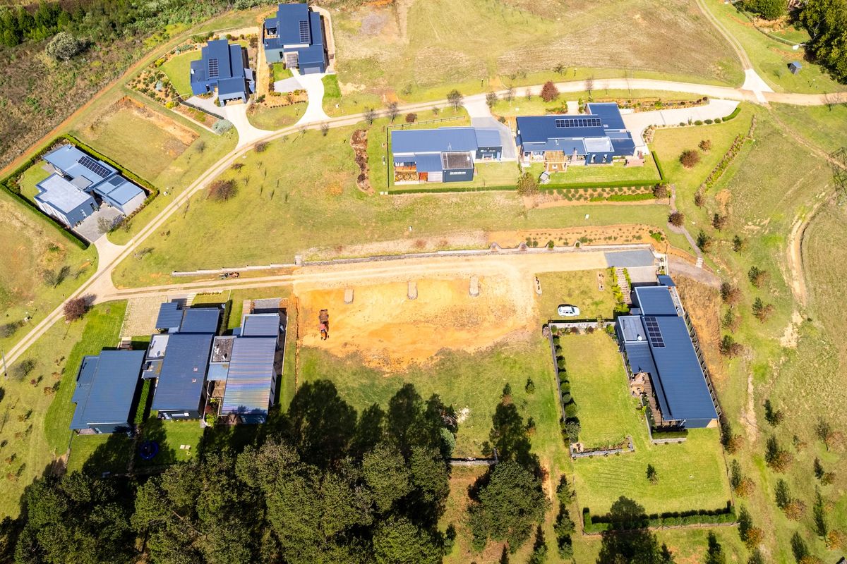 An aerial view of a residential estate featuring vacant land plots surrounded by established modern homes with metal roofing and landscaped grounds.