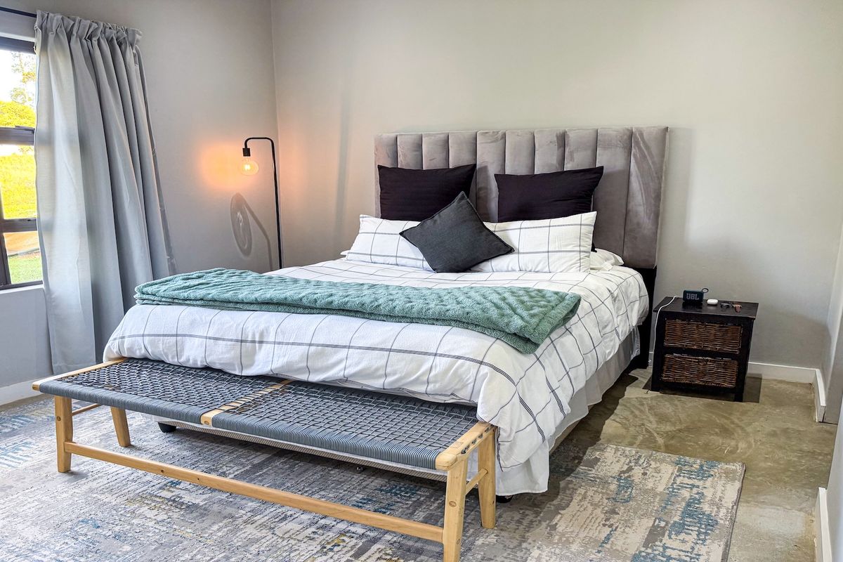 A well-lit bedroom featuring neutral walls, polished concrete flooring, and a large window providing natural light.
