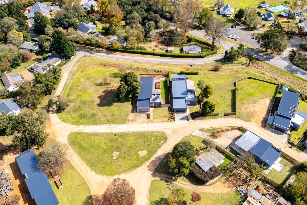 Aerial view of a residential development featuring modern homes with dark metal roofing situated on a spacious, landscaped plot.