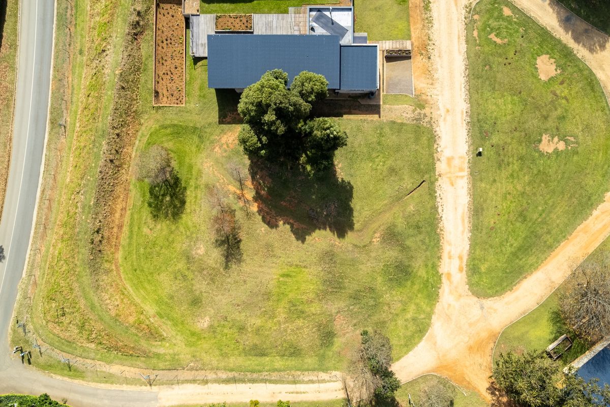 Aerial view of a residential plot featuring a large grassy area, mature trees, and an existing structure with a metal roof.