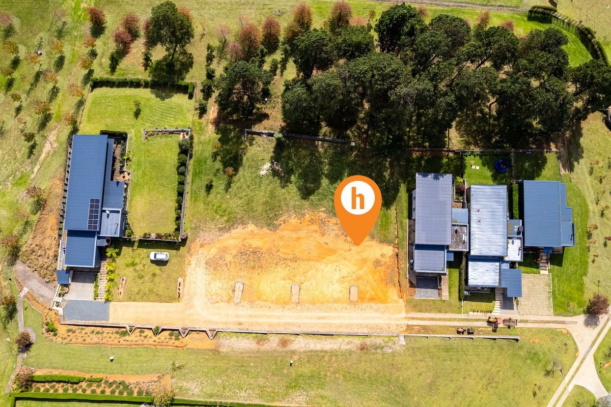 An aerial view of a vacant residential plot situated between two existing properties, featuring cleared land ready for development.