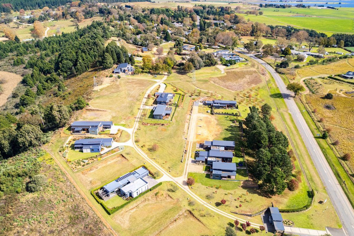 An aerial view of a residential estate featuring multiple modern homes situated on spacious, landscaped plots with surrounding natural greenery and access roads.