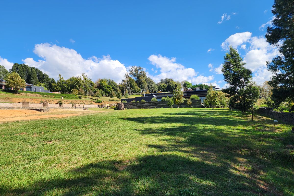 A spacious, well-maintained residential vacant land plot featuring established green lawn, mature trees, and clear boundaries in a scenic setting.