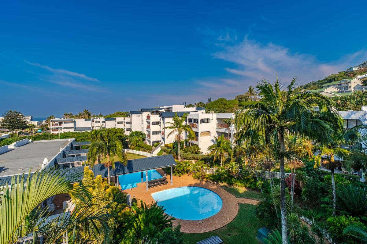 Aerial view of the apartment complex featuring a communal swimming pool, landscaped gardens, and paved outdoor areas.