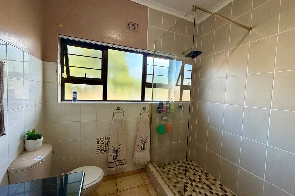 A functional bathroom featuring a walk-in shower with a glass screen, tiled walls, and a window providing natural light.