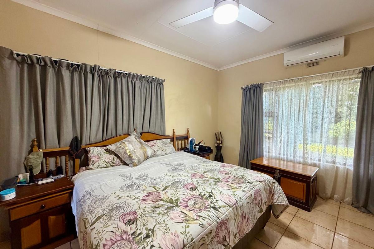 A well-lit bedroom featuring tiled flooring, a ceiling fan, and a wall-mounted air conditioning unit.