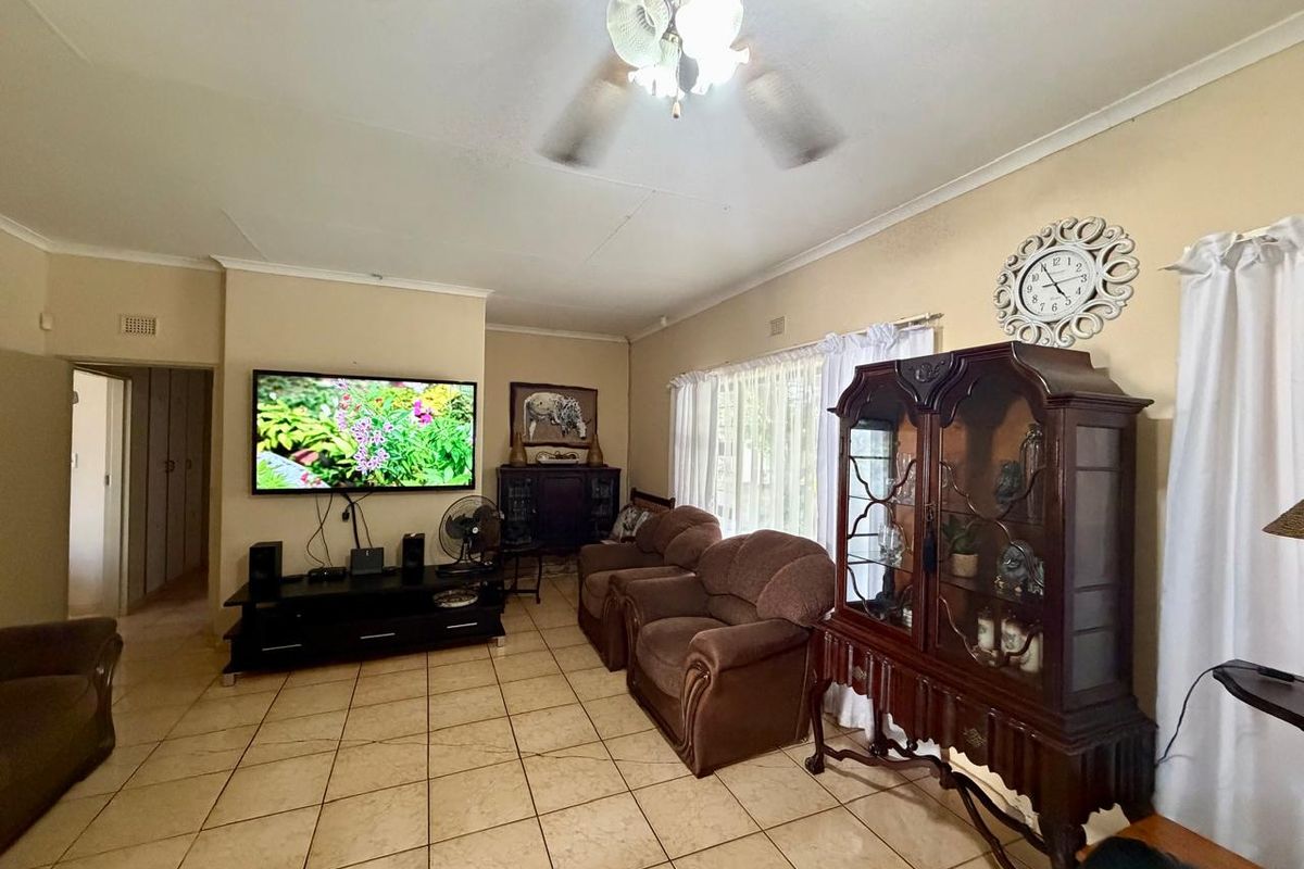A spacious living room featuring tiled flooring, a ceiling fan, and a wall-mounted television setup.