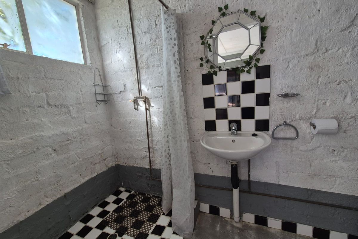 A compact bathroom featuring a shower area with exposed plumbing, a wall-mounted basin, and a black-and-white tiled floor.