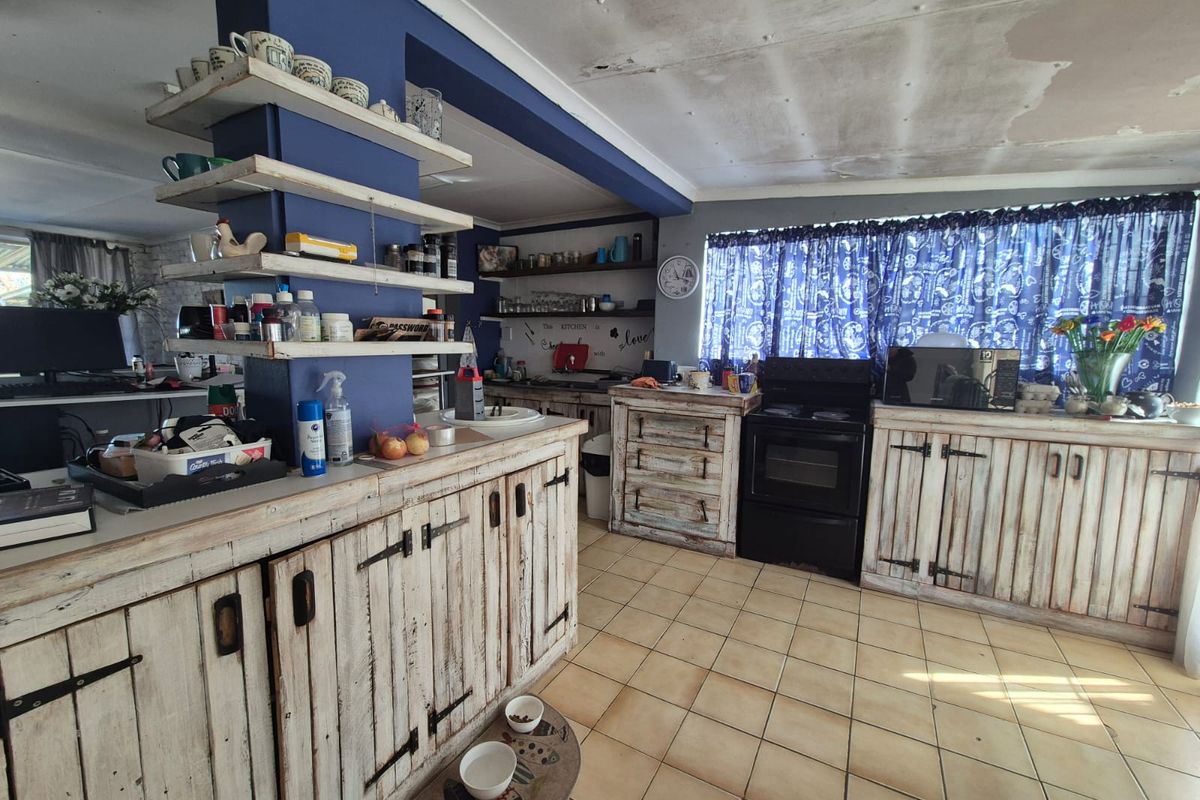 A rustic-style kitchen featuring distressed wooden cabinetry, tiled flooring, and an open-plan layout with a central blue pillar and shelving.