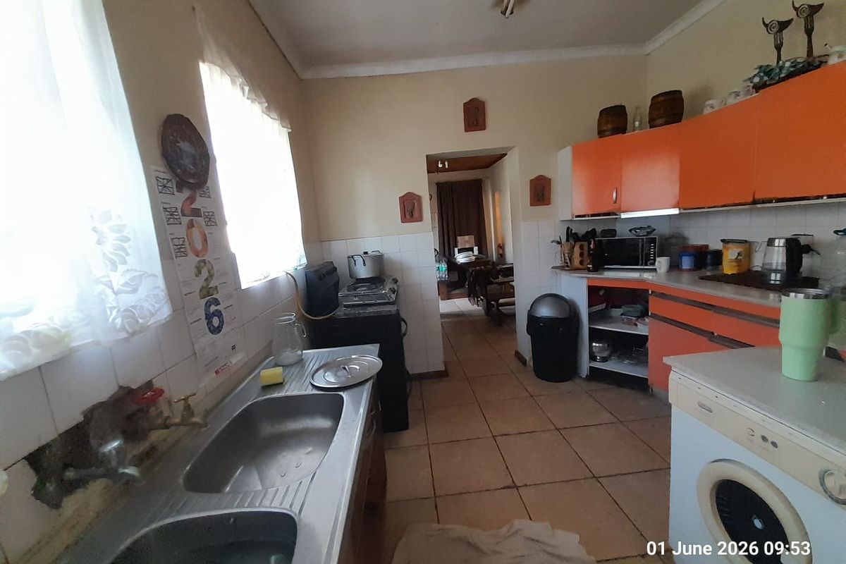 A dated kitchen featuring orange cabinetry, tiled flooring, and a double stainless steel sink, with an adjacent doorway leading to another living area.