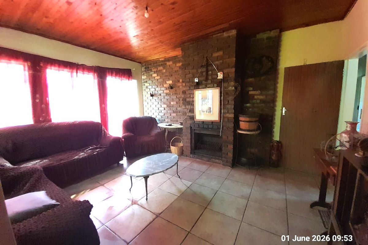 A rustic living room featuring a prominent exposed brick fireplace, tiled flooring, and a warm wood-paneled ceiling, creating a cozy farm-style atmosphere.
