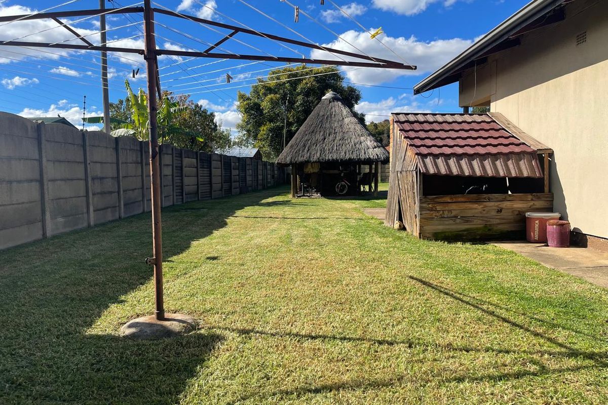 Spacious rear garden featuring a lawn, a traditional thatched lapa, and a small wooden storage structure.