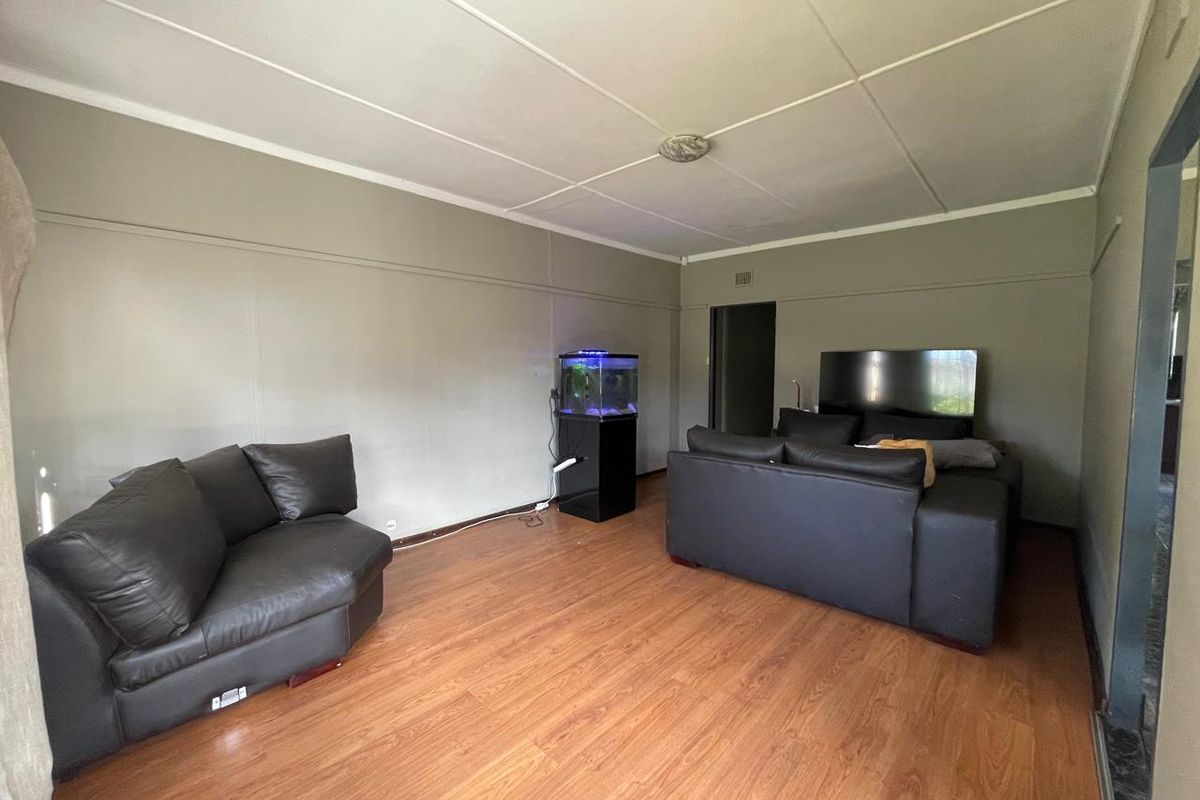 A living room featuring laminate wood flooring and a panelled ceiling, providing a functional and neutral space for relaxation.