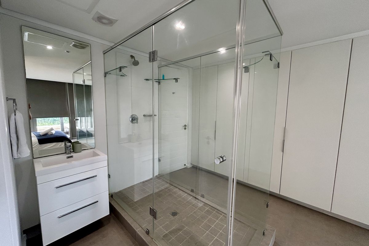Modern bathroom featuring a spacious glass-enclosed shower, wall-mounted vanity with integrated basin, and ample built-in storage cabinetry.