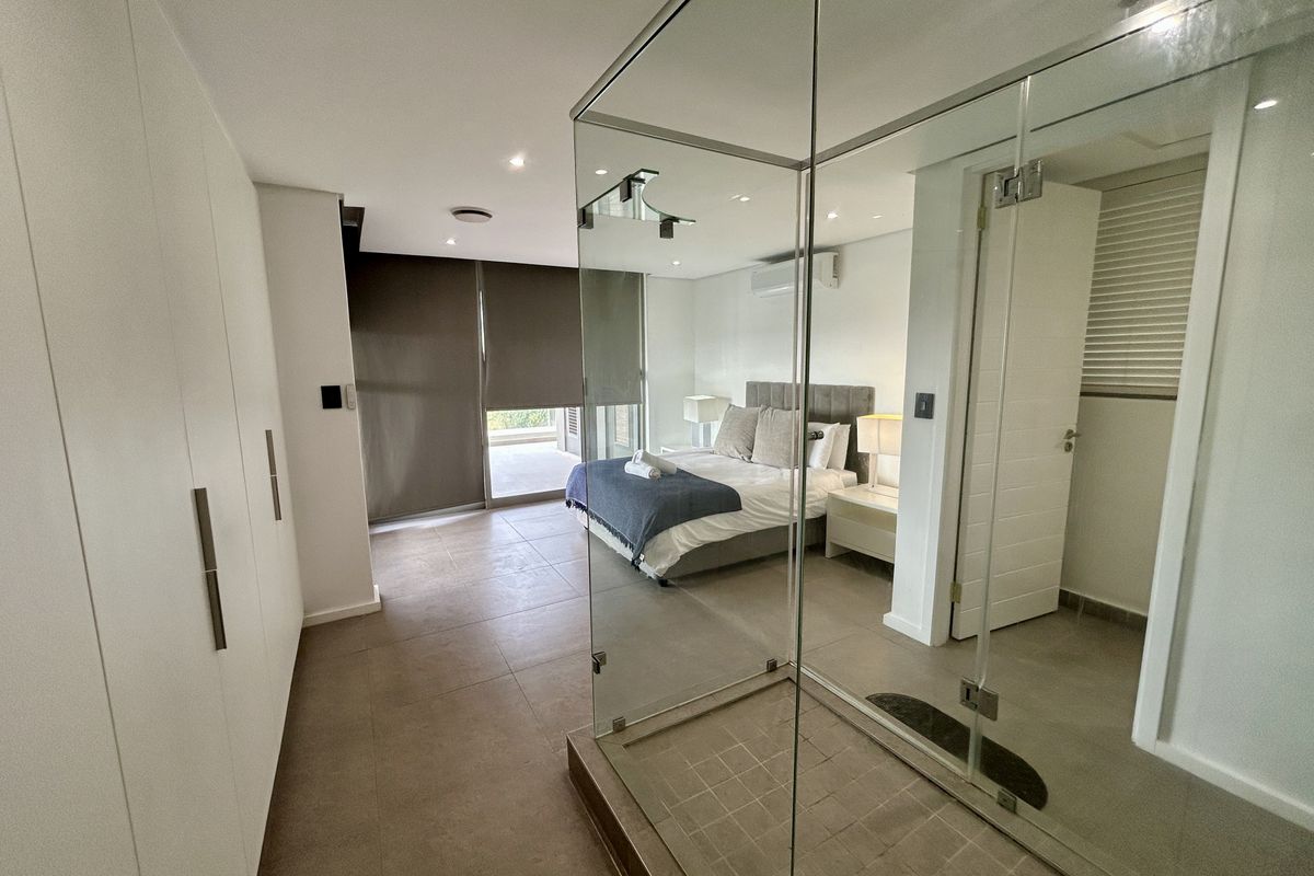 Modern bedroom featuring tiled floors, built-in cupboards, and a unique glass-enclosed shower integrated into the room layout, with access to a private balcony.