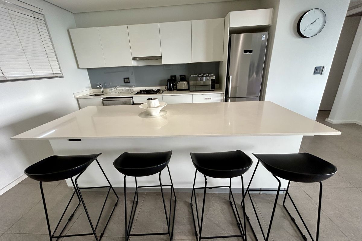 Modern kitchen featuring a large quartz island, sleek white cabinetry, gas hob, and integrated appliances, finished with neutral floor tiles.
