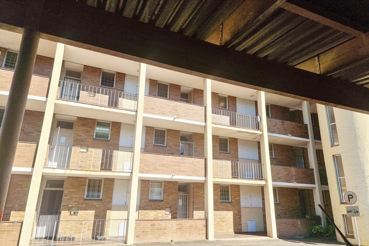 Exterior view of a multi-story townhouse complex featuring face-brick facade, private balconies with metal railings, and a covered parking structure.