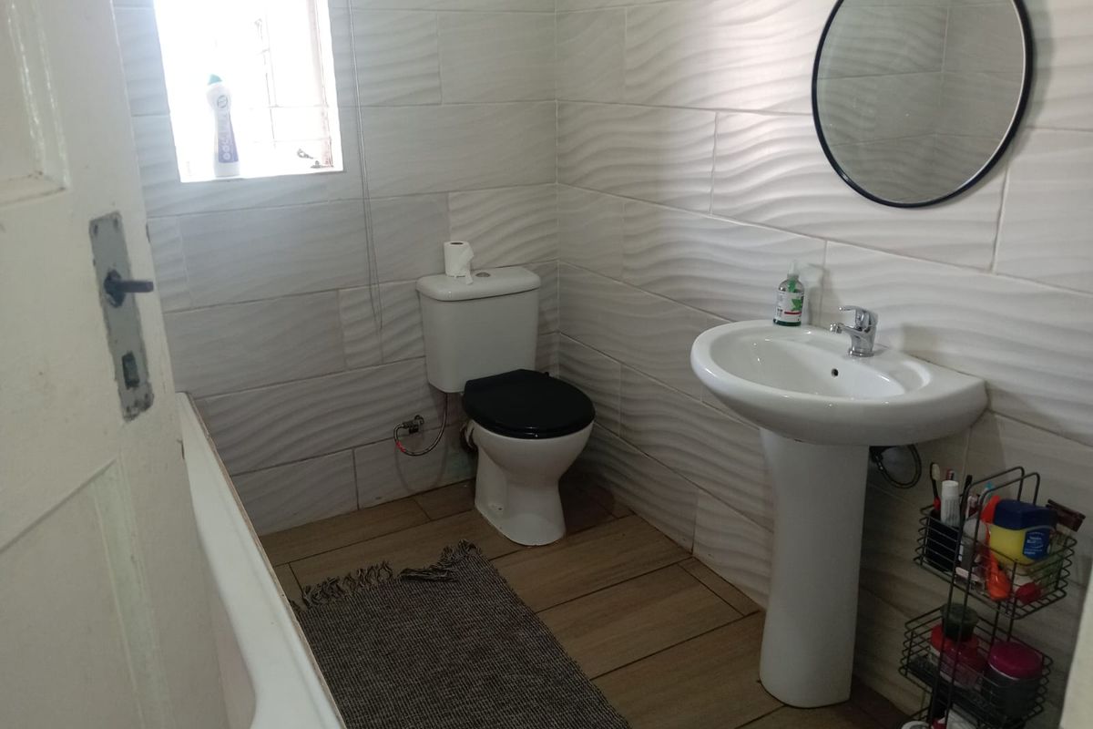 A functional bathroom featuring a pedestal basin, toilet, and tiled walls with a textured finish, providing a clean and practical space.