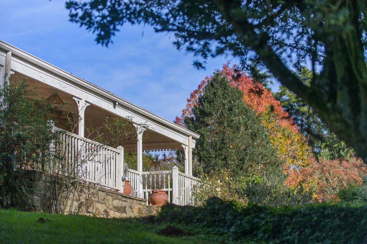 A view of the rear exterior of the property featuring a covered veranda with white timber railings and stone base masonry.