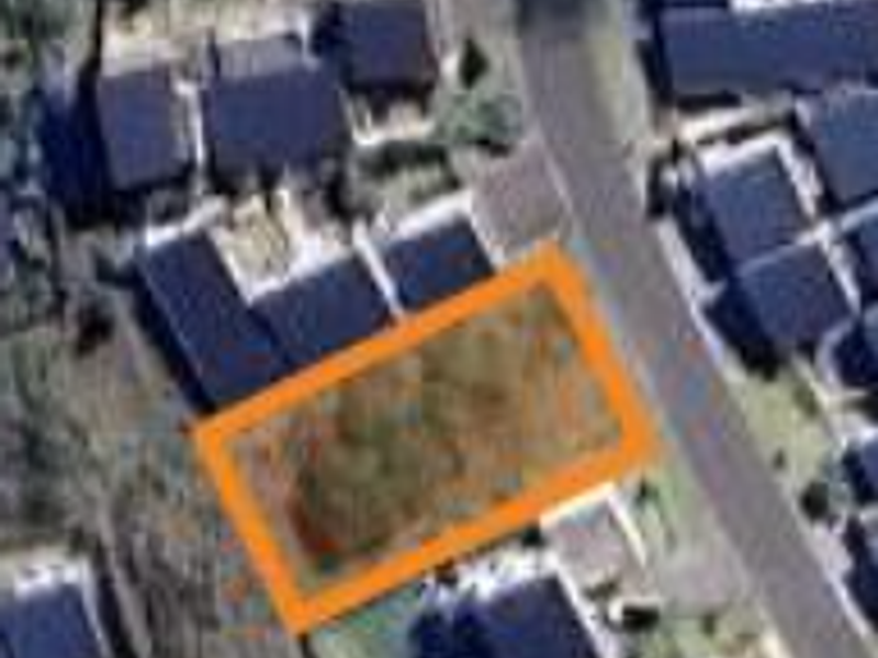 An aerial view of a vacant residential plot highlighted in orange, situated within an established suburban neighborhood.