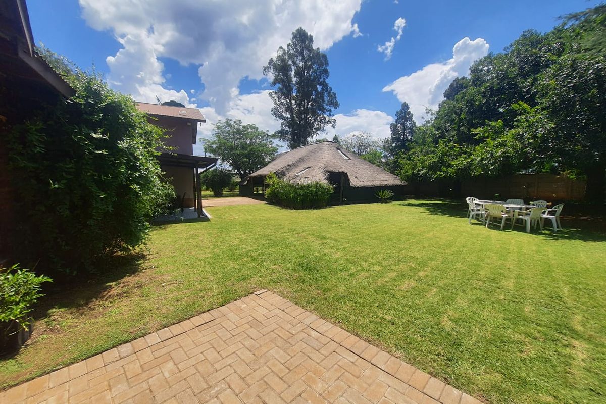 Spacious rear garden featuring a paved patio area, well-maintained lawn, and a detached thatched-roof structure in the background.