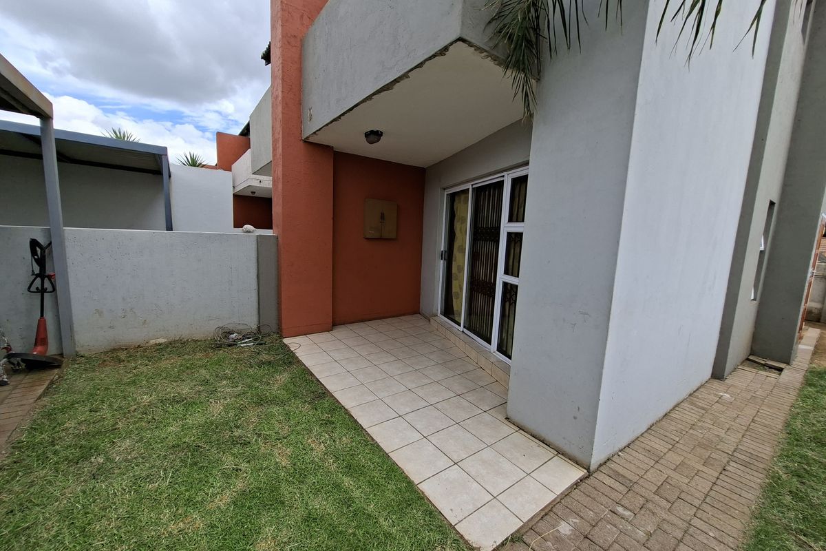 Rear exterior view of the townhouse featuring a tiled patio, sliding glass door with security gate, and a small private garden area.