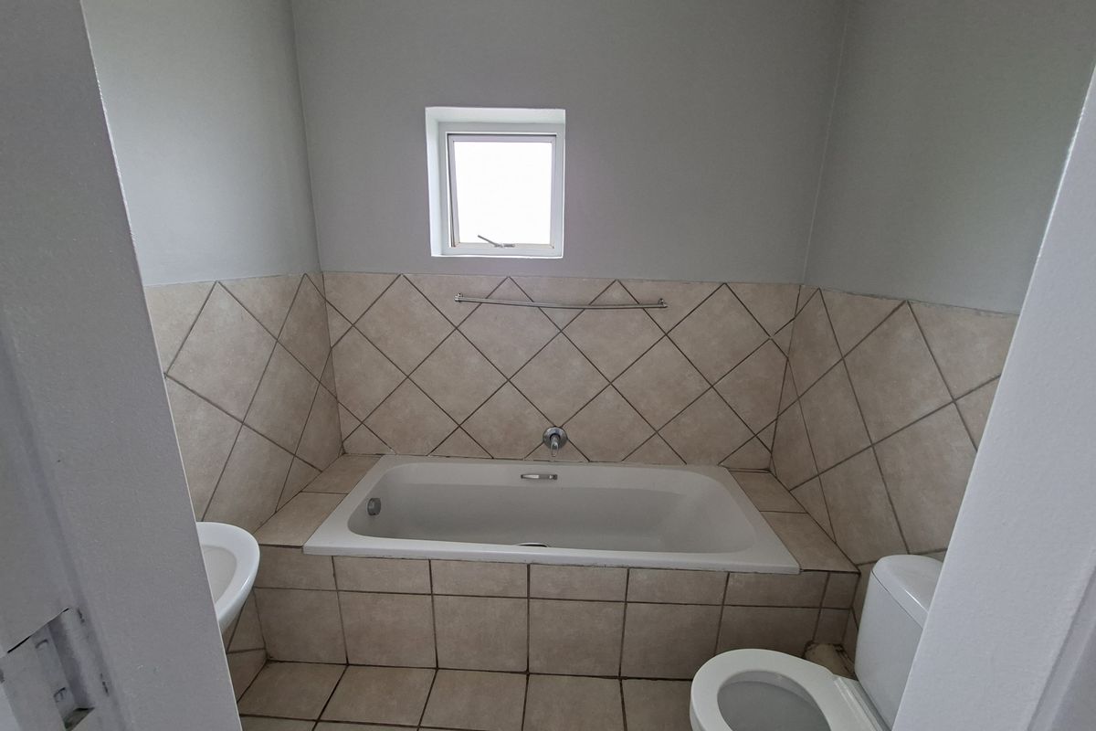 A functional bathroom featuring a built-in bathtub with tiled surround, a toilet, and a washbasin, finished with neutral ceramic wall and floor tiles.