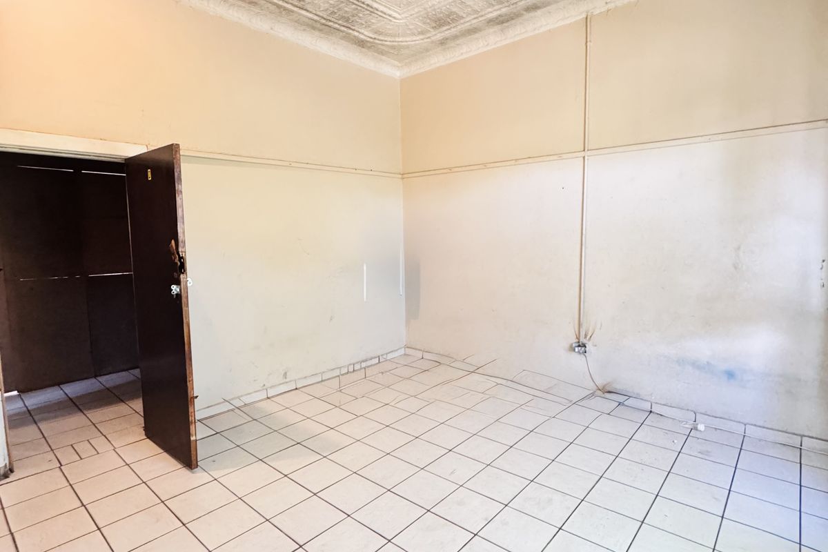 An empty room featuring a decorative pressed metal ceiling, tiled flooring, and a doorway leading to an adjacent space.