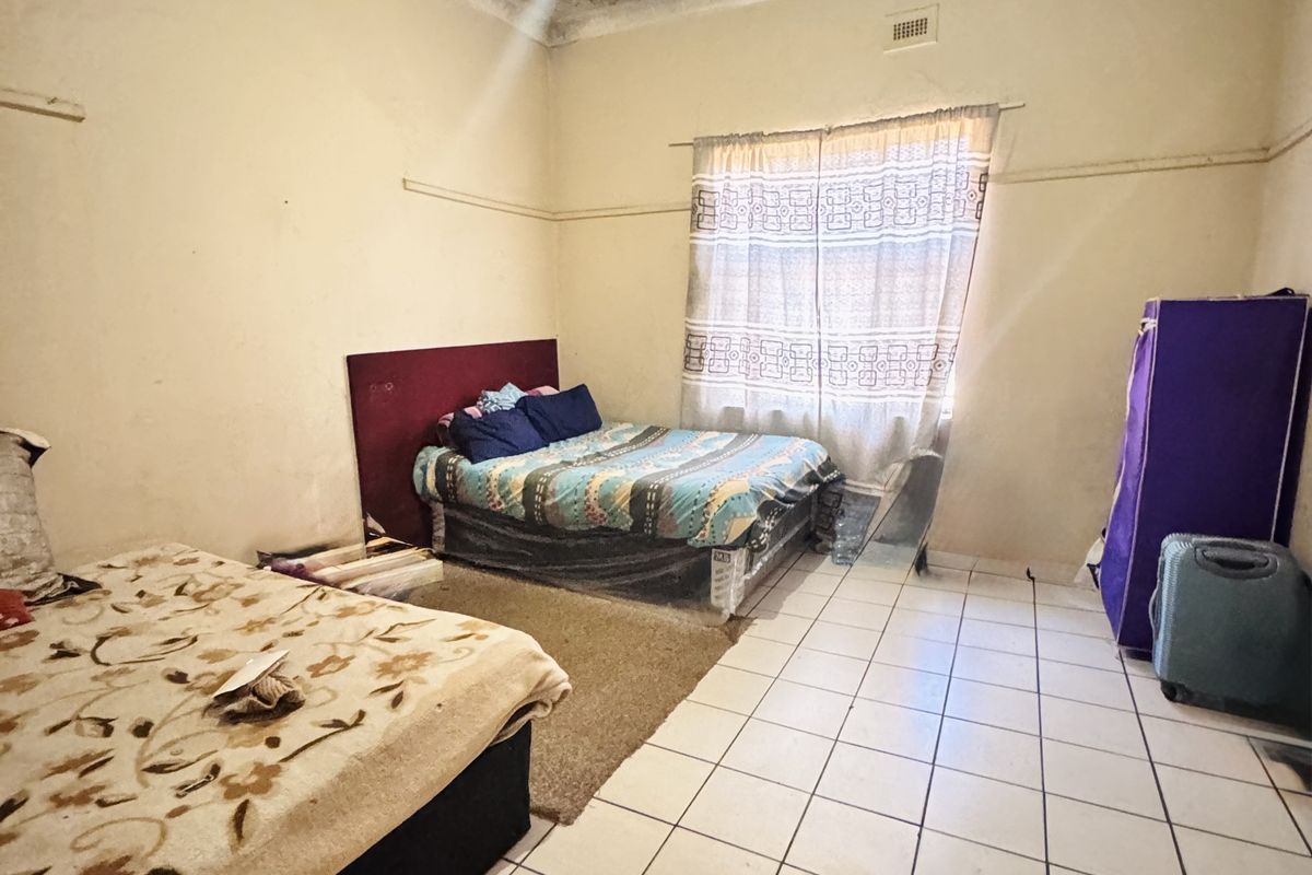 A bedroom featuring tiled flooring and a decorative pressed metal ceiling that shows signs of significant wear and damage.