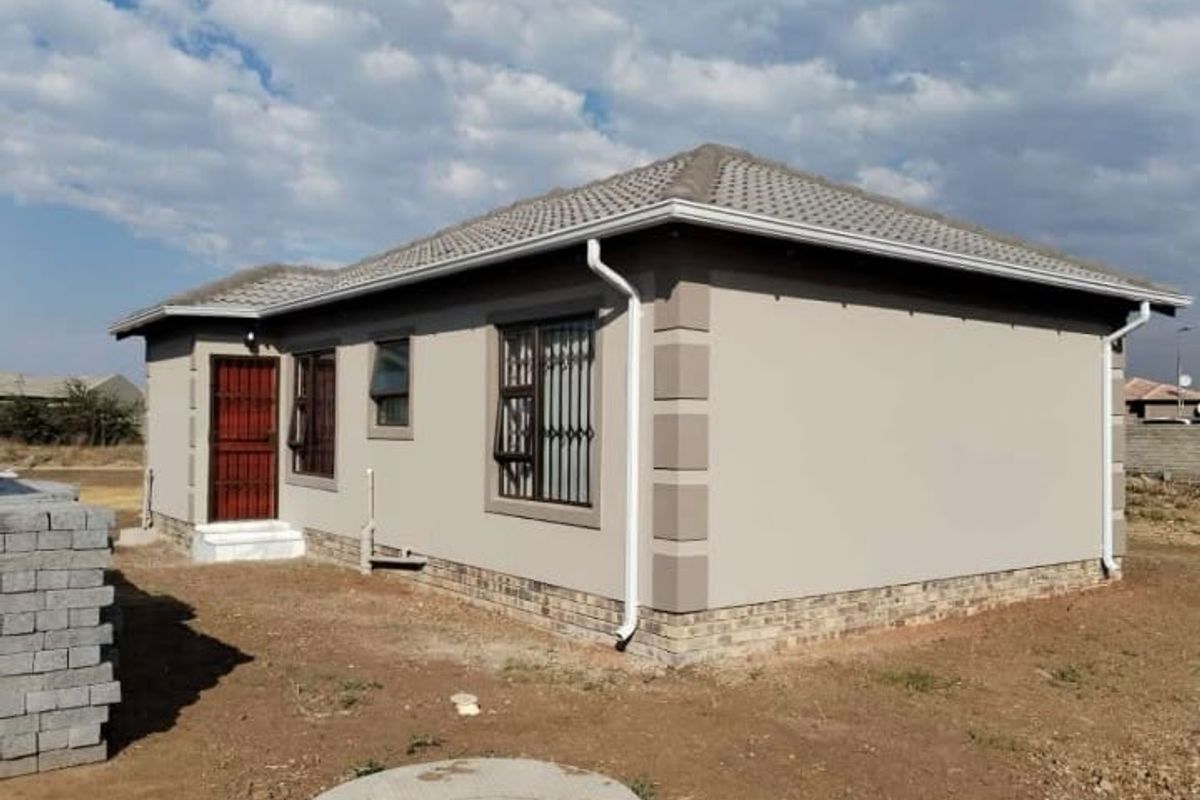 Exterior view of a modern single-story house featuring a tiled roof, painted plaster walls with brick base detailing, and security bars on windows.