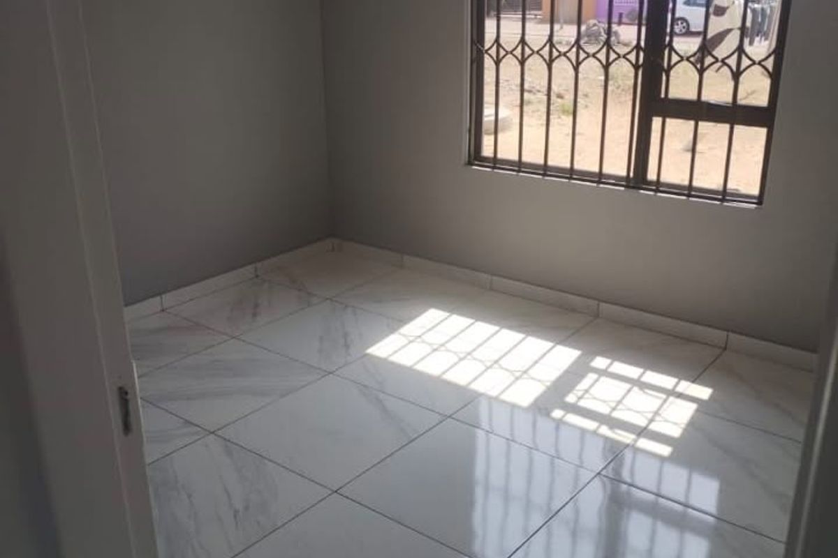 A bright, empty bedroom featuring modern marble-look floor tiles and a window fitted with security burglar bars.