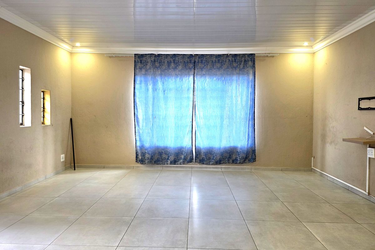 Spacious living area featuring neutral floor tiles, a glossy PVC ceiling, and natural light through large windows.