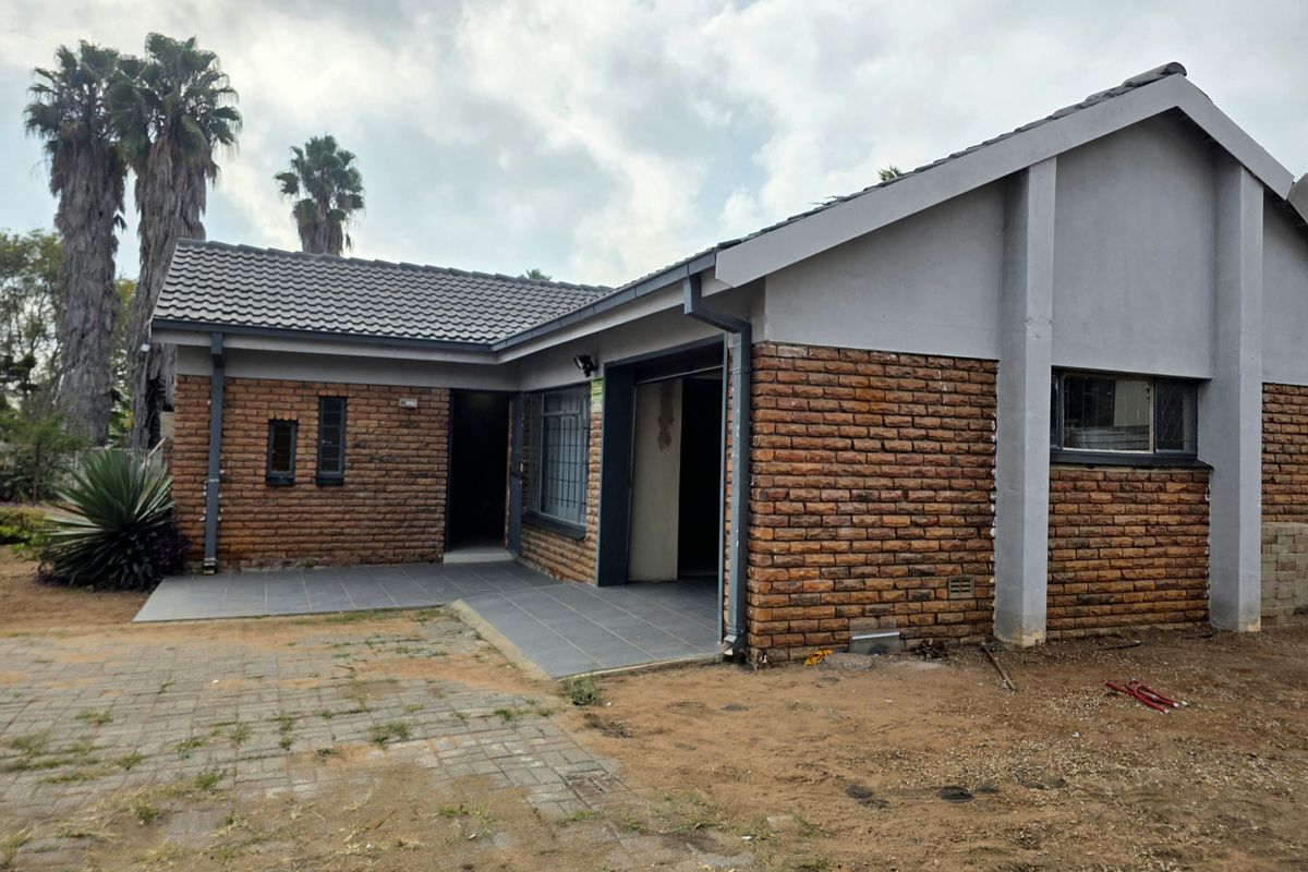 Exterior view of a single-story brick house featuring a tiled roof, paved patio area, and surrounding garden space.