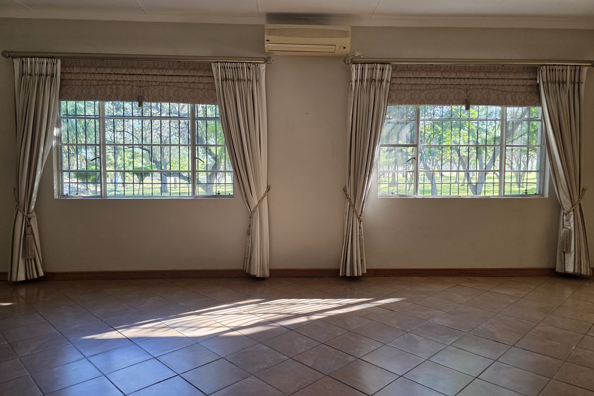 Spacious living area featuring tiled flooring, large windows with security bars, and a wall-mounted air conditioning unit.