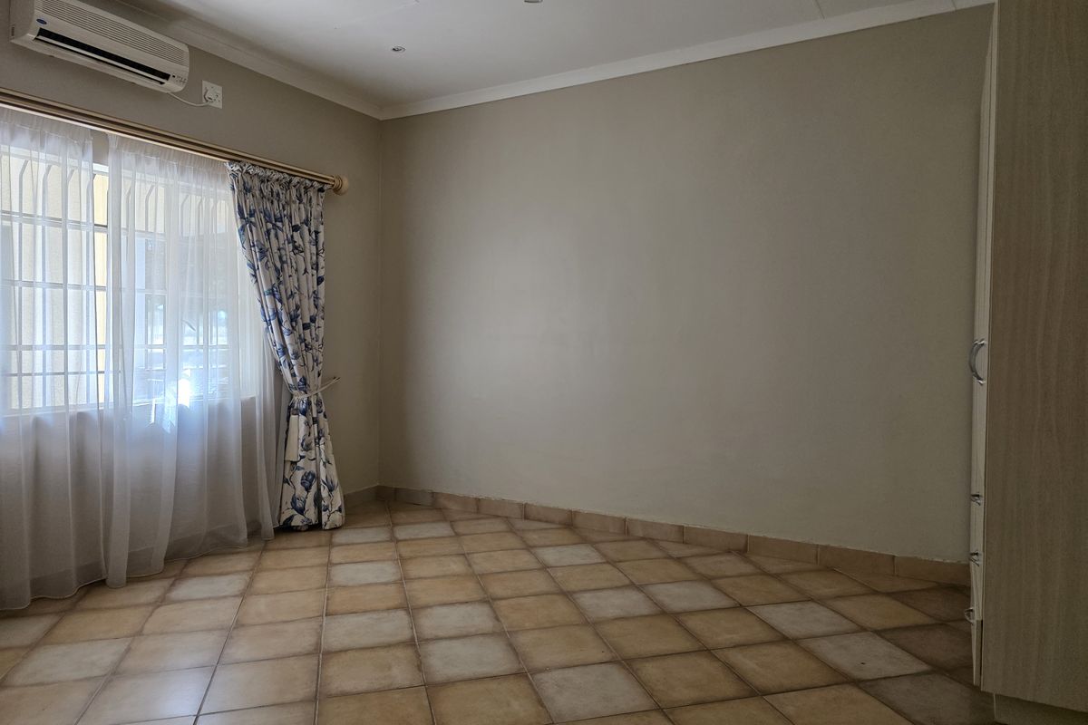 A spacious bedroom featuring tiled flooring, a built-in wardrobe, and a wall-mounted air conditioning unit.